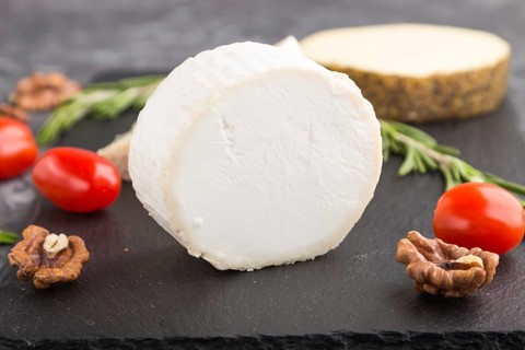 White goat cheese and various types of cheese with rosemary and tomatoes on black slate board on a