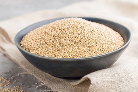 Blue ceramic bowl with raw white quinoa seeds on a gray concrete background and linen textile. Side