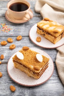 Honey cake with milk cream, caramel, almonds and a cup of coffee on a gray wooden background and