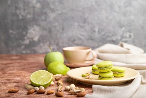 Green macarons or macaroons cakes with cup of coffee on a brown and gray concrete background and