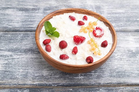 Rice flakes porridge with milk and strawberry in wooden bowl on gray wooden background. Side view,