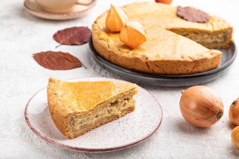 Autumn onion pie decorated with leaves and cup of coffee on gray concrete background. Side view,