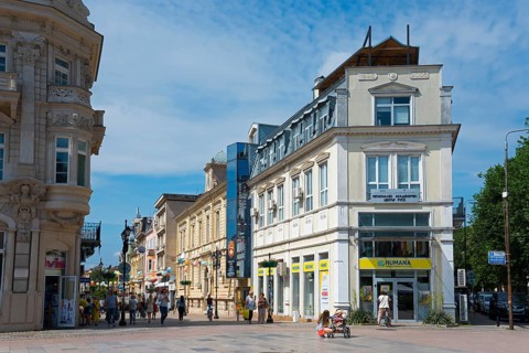 Sunny city scene with people walking on a street between traditional buildings, pedestrian zone