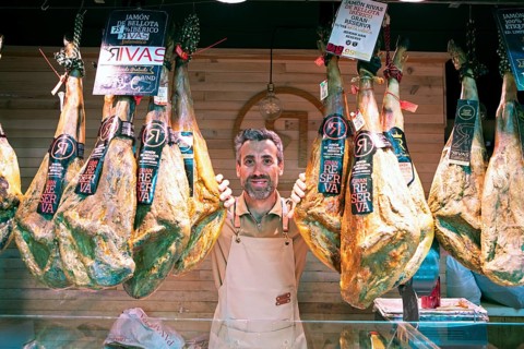 Castilian man, 40 years old, between Iberico hams for sale at the Mercado Central, Salamanca,