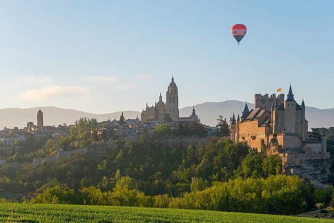 Beautiful view of a castle at sunrise with a hot air balloon in the sky and green fields in the