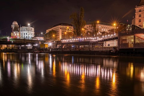 Lights are reflected in the Danube Canal, in the background the illuminated Urania observatory,