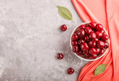 Fresh red sweet cherry in white bowl on gray background with red textile. top view, flat lay, copy
