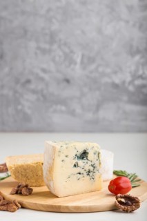 Blue cheese and various types of cheese with rosemary and tomatoes on wooden board on a white and