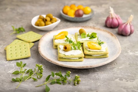 Green cracker sandwiches with cream cheese and cherry tomatoes on gray concrete background. side