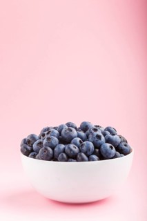 Fresh blueberry in white bowl on pink background. side view, copy space