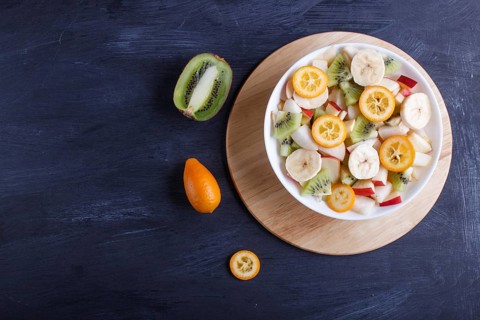 Vegetarian salad of bananas, apples, pears, kumquats and kiwi on black woodem background, top view,