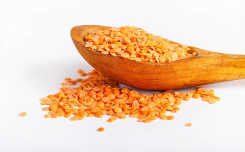 Pile of red lentils in a wooden spoon isolated on white background. Closeup