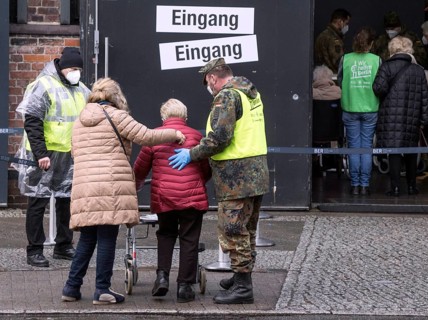 A Bundeswehr soldier helps an elderly woman arriving at the vaccination centre in the Arena in
