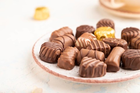Chocolate candies with cup of coffee and hydrangea flowers on a white concrete background. side