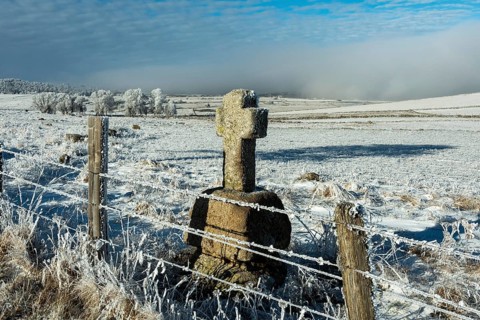 Aubrac plateau in winter. Stone cross at the side of a path. Lozere department. Occitanie. France