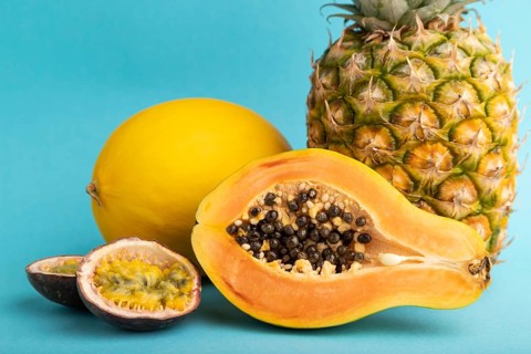 Ripe cut papaya, pineapple, melon, passion fruit, on blue pastel background. Side view, close up.