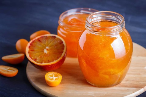 Orange and kumquat jam in a glass jar with fresh fruits on a wooden kitchen board. Homemade, close