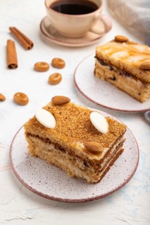 Honey cake with milk cream, caramel, almonds and a cup of coffee on a white concrete background and