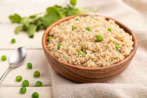 Quinoa porridge with green pea in wooden bowl on a white wooden background and linen textile. Side
