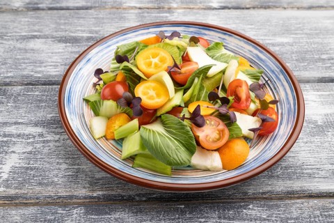 Vegetarian salad of pac choi cabbage, kiwi, tomatoes, kumquat, microgreen sprouts on gray wooden