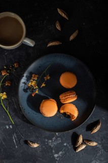 Orange macarons or macaroons cakes with cup of coffee on a black concrete background. Hard light,