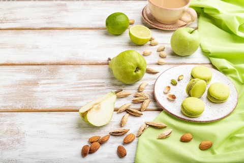 Green macarons or macaroons cakes with cup of coffee on a white wooden background and green linen