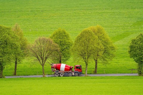 Concrete mixer truck on a country road, green fields, meadows, trees line the 2-lane road, spring,
