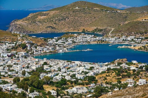 Coastal town with harbour where boats moor, surrounded by green hills and blue water, Skala,