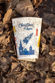 Discarded McDonald's take-away drink carton cup on floor on top of leaf litter, 'Christmas is here'