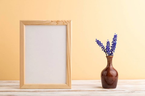 Wooden frame with blue muscari hyacinth flowers in ceramic vase on orange pastel background. side
