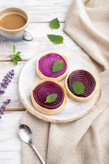 Sweet tartlets with jelly and milk cream with cup of coffee on a white wooden background and linen