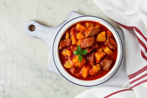 Potatoes stewed with meat, in tomato sauce, with spices and herbs, no people, on a white table