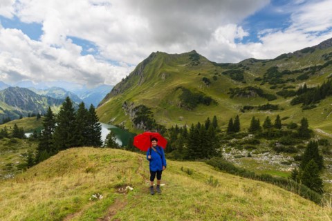 Woman 60-65 hiking with umbrella, behind her Seealpsee and Seeköpfel, 1919m, Allgäu Alps, Allgäu,