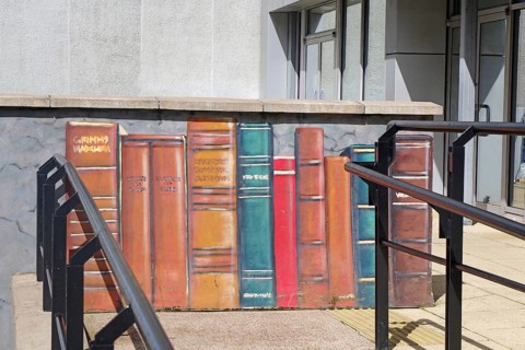 A mural shows colourful books lined up on a wall in the city, Mural Trail, Glasgow, Scotland,