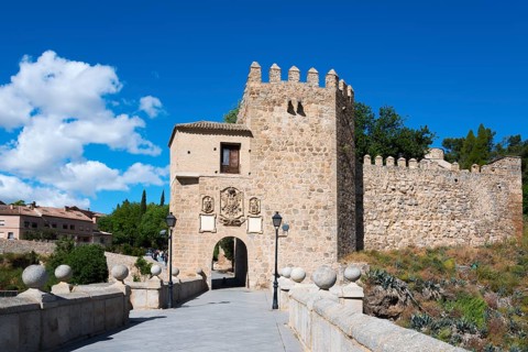 Old stone castle with neighbouring bridge under a blue sky, surrounded by green plants, Puente de