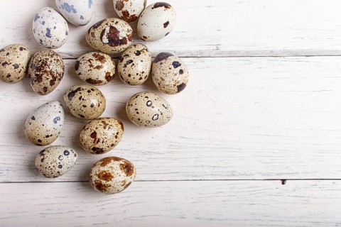 Raw quail eggs on a white wooden background, top view