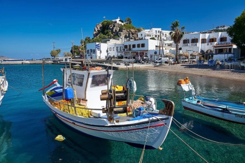 A white fishing boat moored at a Greek island harbour with crystal clear water and historic