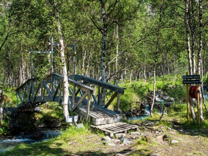 Wooden bridge on hiking path crosses a small river, hike along valley Steindalen to glacier