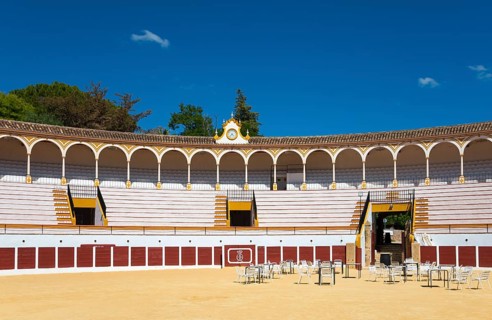 Historic bullring with classic architecture and blue sky, sandy floor and chairs in the centre,