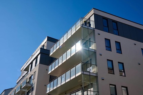 Modern residential building with glass balconies under a blue sky and reflecting sunlight, Molde,