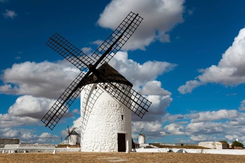 Historic white windmill under a blue sky with clouds and sunny surroundings in a wide landscape,