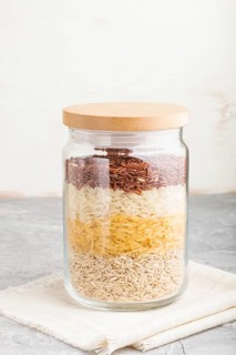 Glass jar with different kinds of rice poured in layers on a gray and white background. side view,