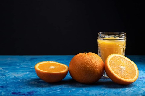 Glass of orange juice on a black and blue background. Hard light, contrast. Side view, copy space