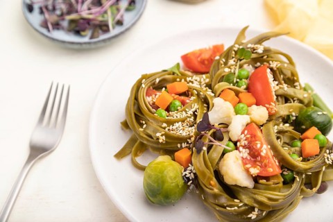Tagliatelle green spinach pasta with tomato, pea and microgreen sprouts on a white wooden