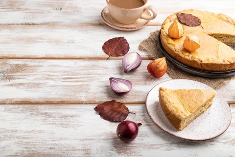 Autumn onion pie decorated with leaves and cup of coffee on white wooden background and linen