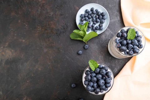 Yogurt with blueberry and chia in glass on black concrete background and orange linen textile. top