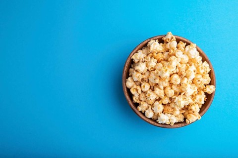 Popcorn with caramel in wooden bowl on a pastel blue background. Top view, flat lay, copy space