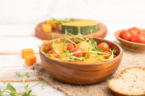 Vegetarian vegetable salad of tomatoes, pumpkin, microgreen pea sprouts on white wooden background