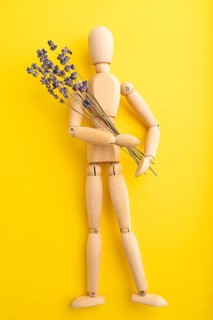 Wooden mannequin holding lavender flowers on yellow pastel background. close up, isolated, summer,