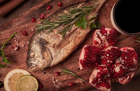 Fried dorado fish, with spices and herbs, on a wooden board, pomegranate sauce, close-up, no people